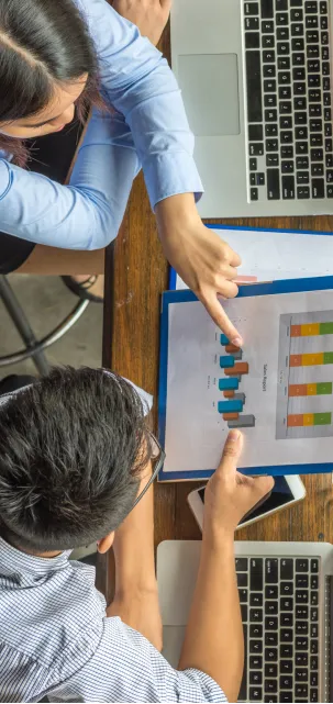 Vue de dessus de deux personnes analysant un rapport de ventes imprimé avec des graphiques